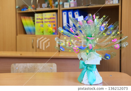 Bouquet crafted from recycled plastic bottles, featuring colorful flowers and vibrant decorations, displayed on a wooden table in a classroom setting promoting sustainability and creativity 136212073