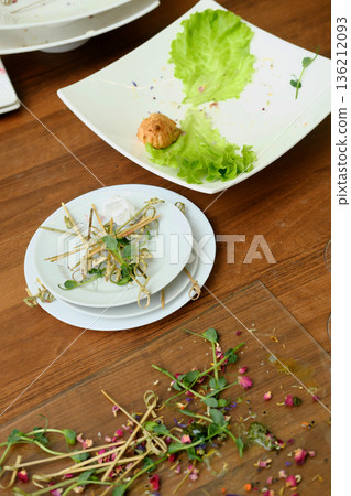 Dirty dishes piled on a wooden table after a banquet, featuring leftover food, wilted greens, and remnants of a lavish reception, showcasing the aftermath of a festive gathering Dirty dishes piled on a wooden table after a banquet, featuring leftover food, wilted greens, and remnants of a lavish reception, showcasing the aftermath of a festive gathering 136212093