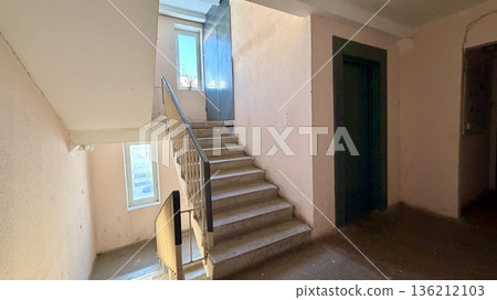 Residential apartment building stairwell with concrete stairs, metal railings and windows 136212103