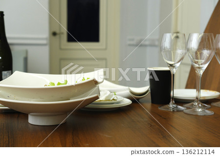 Elegant dining table setting featuring white ceramic bowls, wine glasses, and a black cup, creating a sophisticated atmosphere for a meal or gathering Elegant dining table setting featuring white ceramic bowls, wine glasses, and a black cup, creating a sophisticated atmosphere for a meal or gathering 136212114