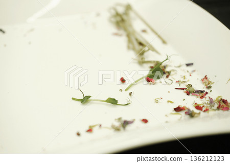 Leftover food remnants on a white plate, featuring scattered herbs and colorful flower petals, illustrating the concept of food waste and its environmental impact Leftover food remnants on a white plate, featuring scattered herbs and colorful flower petals, illustrating the concept of food waste and its environmental impact 136212123
