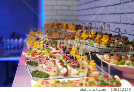 Colorful catering display featuring an array of gourmet snacks and appetizers elegantly arranged on platters, illuminated by evening lighting with a vibrant atmosphere Colorful catering display featuring an array of gourmet snacks and appetizers elegantly arranged on platters, illuminated by evening lighting with a vibrant atmosphere 136212136