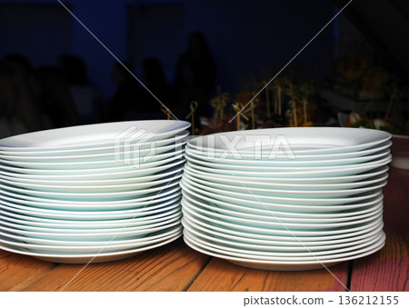 Stacked white plates with subtle green rims are arranged neatly on a wooden table, showcasing elegant tableware design and preparation for dining experience Stacked white plates with subtle green rims are arranged neatly on a wooden table, showcasing elegant tableware design and preparation for dining experience 136212155