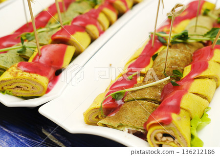 Colorful rolled crepes filled with savory ingredients, garnished with vibrant sauces and herbs, presented elegantly on a white platter, showcasing culinary artistry and creativity 136212186