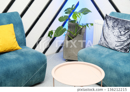 Modern living room featuring two stylish blue chairs, a pink coffee table, and a concrete planter with lush green plants, creating a cozy and inviting atmosphere 136212215