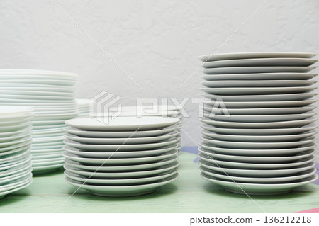 Stacked white plates arranged neatly on a colorful table, showcasing the organization and preparation for catering services in a vibrant food service environment Stacked white plates arranged neatly on a colorful table, showcasing the organization and preparation for catering services in a vibrant food service environment 136212218