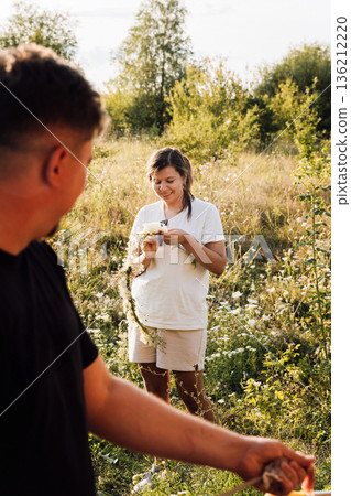 Woman making wildflower wreath in sunny meadow, romantic summer outdoors 136212220