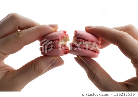 Close-up of hands gently breaking a pink macaron in half, revealing a creamy filling. Perfect for food blogs, patisserie ads, and delicate dessert concepts Close-up of hands gently breaking a pink macaron in half, revealing a creamy filling. Perfect for food blogs, patisserie ads, and delicate dessert concepts 136212539