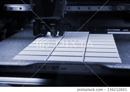 3D printer close up. Working 3D printer in process of printing object from molten white plastic. 3D printer creating model by flowing liquid plastic from extruder of printer. 3D printing technology 136212601