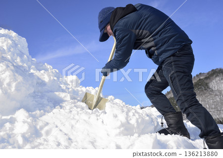 An elderly man living in a rural area with heavy snowfall is clearing snow 136213880