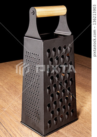 Black grater for shredding vegetables set on a wooden kitchen table Black grater for shredding vegetables set on a wooden kitchen table 136213903