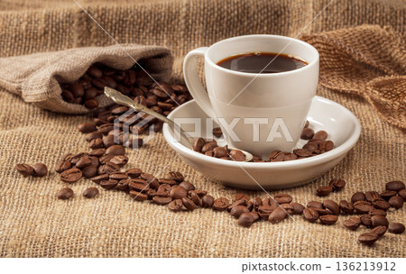 Warm and inviting coffee scene: cup with coffee beans on burlap background Warm and inviting coffee scene: cup with coffee beans on burlap background 136213912