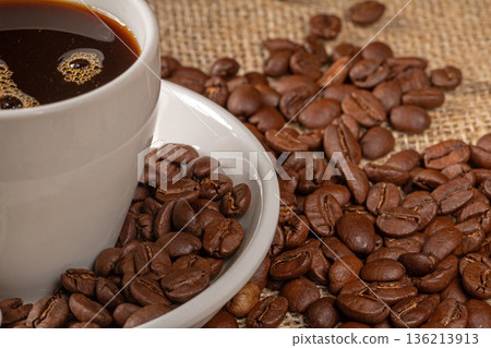 A beautiful cup of coffee surrounded by scattered coffee beans on a rustic burlap background 136213913