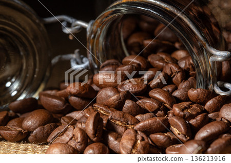 Close-up view of coffee beans pouring from a glass jar, frontal perspective Close-up view of coffee beans pouring from a glass jar, frontal perspective 136213916