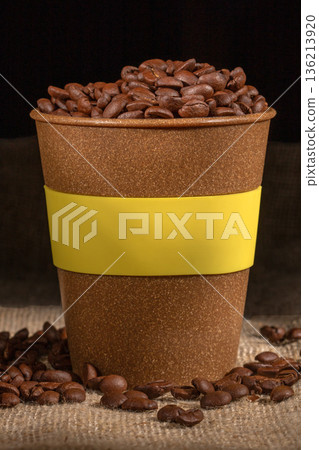 plastic cup overflowing with high-quality coffee beans displayed on a surface 136213920