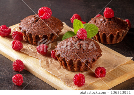 Freshly baked muffins surrounded by juicy raspberries on a black kitchen table Freshly baked muffins surrounded by juicy raspberries on a black kitchen table 136213931