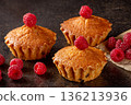 Freshly baked lemon muffins accompanied by juicy raspberries on a rustic kitchen table 136213936