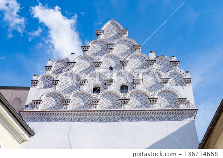 The gable features detailed designs of South Bohemian architecture in Trebon. The structure stands against a bright blue sky. The craft shows skill in building decoration. The gable features detailed designs of South Bohemian architecture in Trebon. The structure stands against a bright blue sky. The craft shows skill in building decoration. 136214668