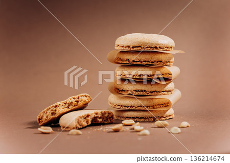 Stacked beige macarons with crumbs and peanuts on brown background copy space Stacked beige macarons with crumbs and peanuts on brown background copy space 136214674