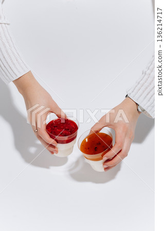 Hands holding two panna cotta cups with berry and passion fruit topping 136214717