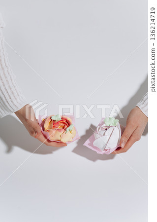 Hands holding pastel meringue swirls on pink paper, minimal white background Hands holding pastel meringue swirls on pink paper, minimal white background 136214719