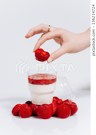 Hand placing strawberry on panna cotta in cup with berries on white background Hand placing strawberry on panna cotta in cup with berries on white background 136214724