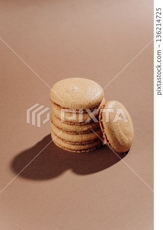 Beige macarons stacked on brown background, minimal French dessert 136214725