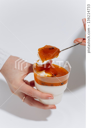 Hand holding panna cotta cup with passion fruit sauce, spoonful on white Hand holding panna cotta cup with passion fruit sauce, spoonful on white 136214733