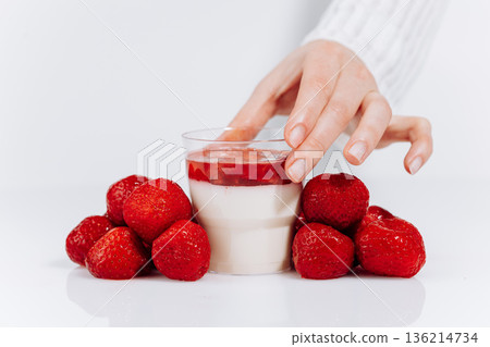 Hand holding strawberry panna cotta dessert cup with fresh berries on white background 136214734