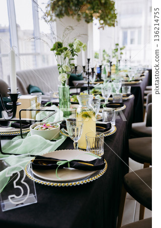 Elegant banquet table with green decor and lemonade pitcher in bright restaurant 136214755