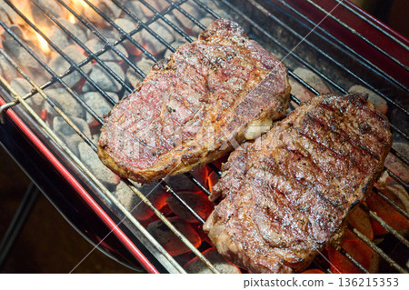 barbecue party, close-up image of grilling steaks, the meat is stewed in butter with garlic and thyme, spiking pieces of meat on the grill, various vegetables, lots of smoke 136215353