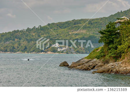 Thailand's coast on a sunny day, villas and hotels among palm trees on a hill, people on a jet ski, a yacht off the coast 136215389