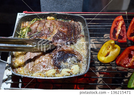 barbecue party, close-up image of grilling steaks, the meat is stewed in butter with garlic and thyme, spiking pieces of meat on the grill, various vegetables, lots of smoke barbecue party, close-up image of grilling steaks, the meat is stewed in butter with garlic and thyme, spiking pieces of meat on the grill, various vegetables, lots of smoke 136215471