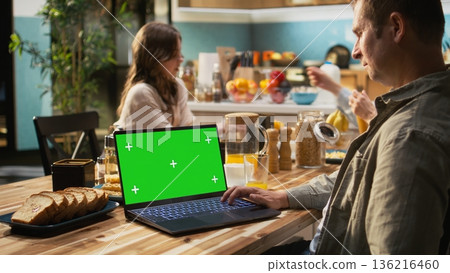 Chroma key on laptop next to mother enjoying breakfast at the kitchen table, plates of scrambled eggs, toast and fruits. Parents and pre-teen girl laugh together with delicious food. Chroma key on laptop next to mother enjoying breakfast at the kitchen table, plates of scrambled eggs, toast and fruits. Parents and pre-teen girl laugh together with delicious food. 136216460