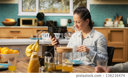 Preoccupied mother being detached and ignoring her family at the table, being distracted with a phone dependency and obsession during breakfast. Social media addiction. 136216474
