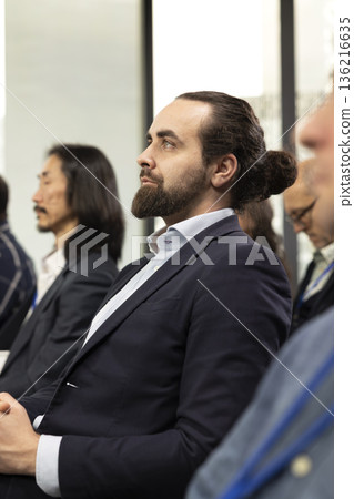 Male CEO attends professional business event in conference room with panel presentation. Listening to speaker promoting leadership and entrepreneurship values among participants. 136216635