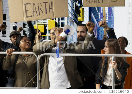 African american man with loudspeaker attend climate strike and manifestation with group of activists and protestors, marching together with posters to defend nature and environmental rights. 136216640