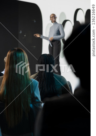 Selective focus of diverse attendees seated during new smartphone launch presentation, product manager introducing new mobile device with sleek design. Modern announcement at summit. Selective focus of diverse attendees seated during new smartphone launch presentation, product manager introducing new mobile device with sleek design. Modern announcement at summit. 136216649