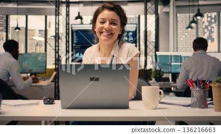 Portrait of businesswoman opening laptop seated at office desk, analyzing charts and graphs during performance review in a professional workspace. Corporate lifestyle with KPI metrics. Portrait of businesswoman opening laptop seated at office desk, analyzing charts and graphs during performance review in a professional workspace. Corporate lifestyle with KPI metrics. 136216663