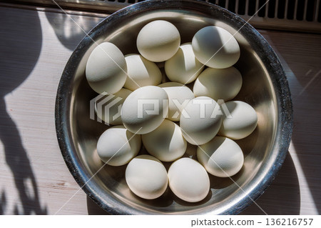 Top view of a metal bowl filled with white eggs ready for easter egg decorating in bright sunlight with strong shadows Top view of a metal bowl filled with white eggs ready for easter egg decorating in bright sunlight with strong shadows 136216757