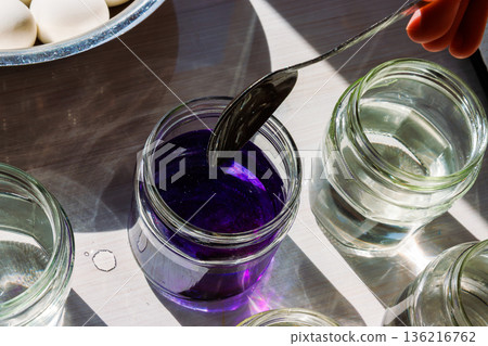 Top view of a glass jar filled with water colored with deep purple food dye being stirred with the spoon on a sunlit table Top view of a glass jar filled with water colored with deep purple food dye being stirred with the spoon on a sunlit table 136216762