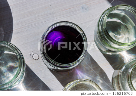 Top view of a jar filled with deep purple food dye solution surrounded by clear water jars in bright sunlight 136216763
