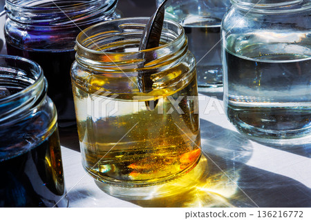 Close up of a glass jar with yellow food dye dissolving in water, while someone is stirring the liquid it with a spoon Close up of a glass jar with yellow food dye dissolving in water, while someone is stirring the liquid it with a spoon 136216772