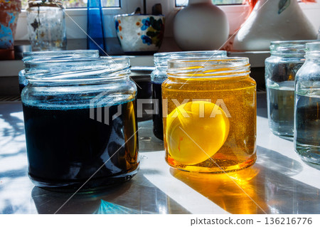 Egg soaking in yellow dye jar beside blue dye jar for easter egg coloring 136216776