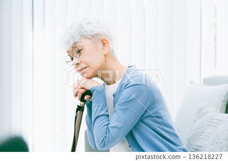 Depressed senior woman with a cane in her hand in the living room Depressed senior woman with a cane in her hand in the living room 136218227