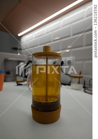Transparent glass tea press brewing yellow herbal tea in a modern kitchen setting 136218592