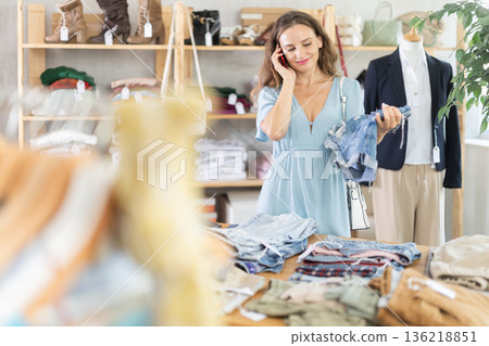 woman in a summer dress chooses jeans and calls on her cell phone 136218851
