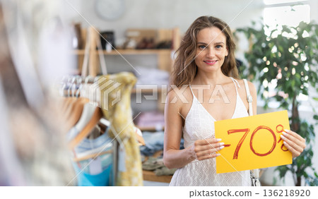 Young woman holding discount sign in clothing store Young woman holding discount sign in clothing store 136218920