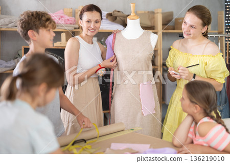 Woman teacher uses mannequin during sewing lesson with children Woman teacher uses mannequin during sewing lesson with children 136219010