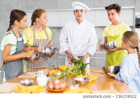 Young guy cook teaches to cook group of children Young guy cook teaches to cook group of children 136219022